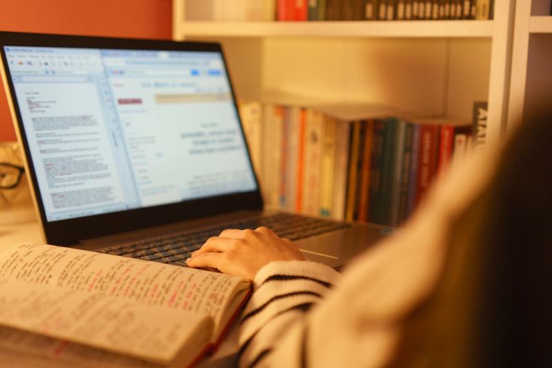 Person reading reference material on a laptop beside books